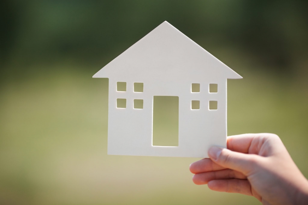 Close-up shot of female hands holding small house model on the background of defocused green nature. Real estate, mortgage, eco or country house concept